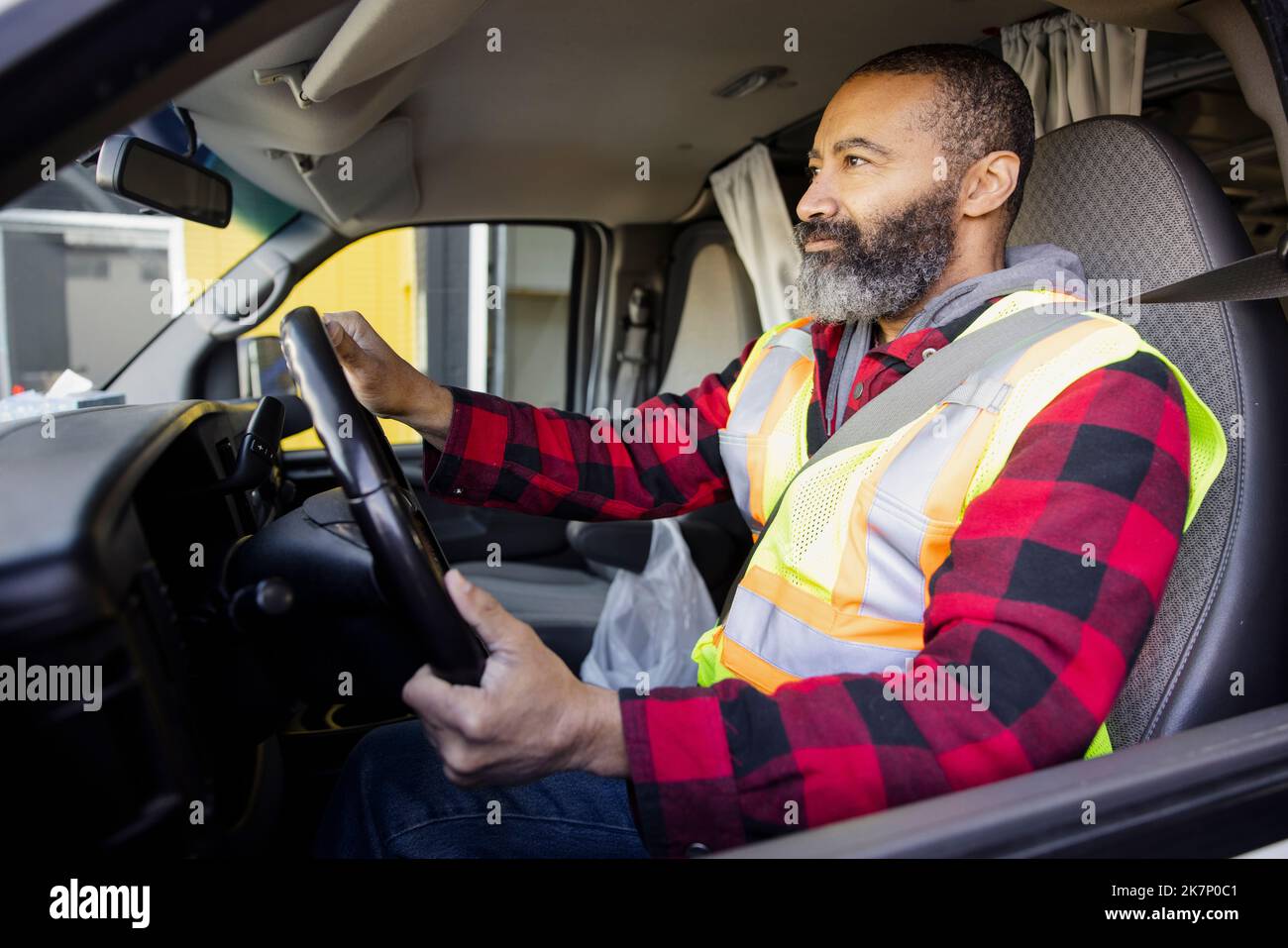 Hombre trabajador en chaleco reflectante que conduce la furgoneta Foto de stock