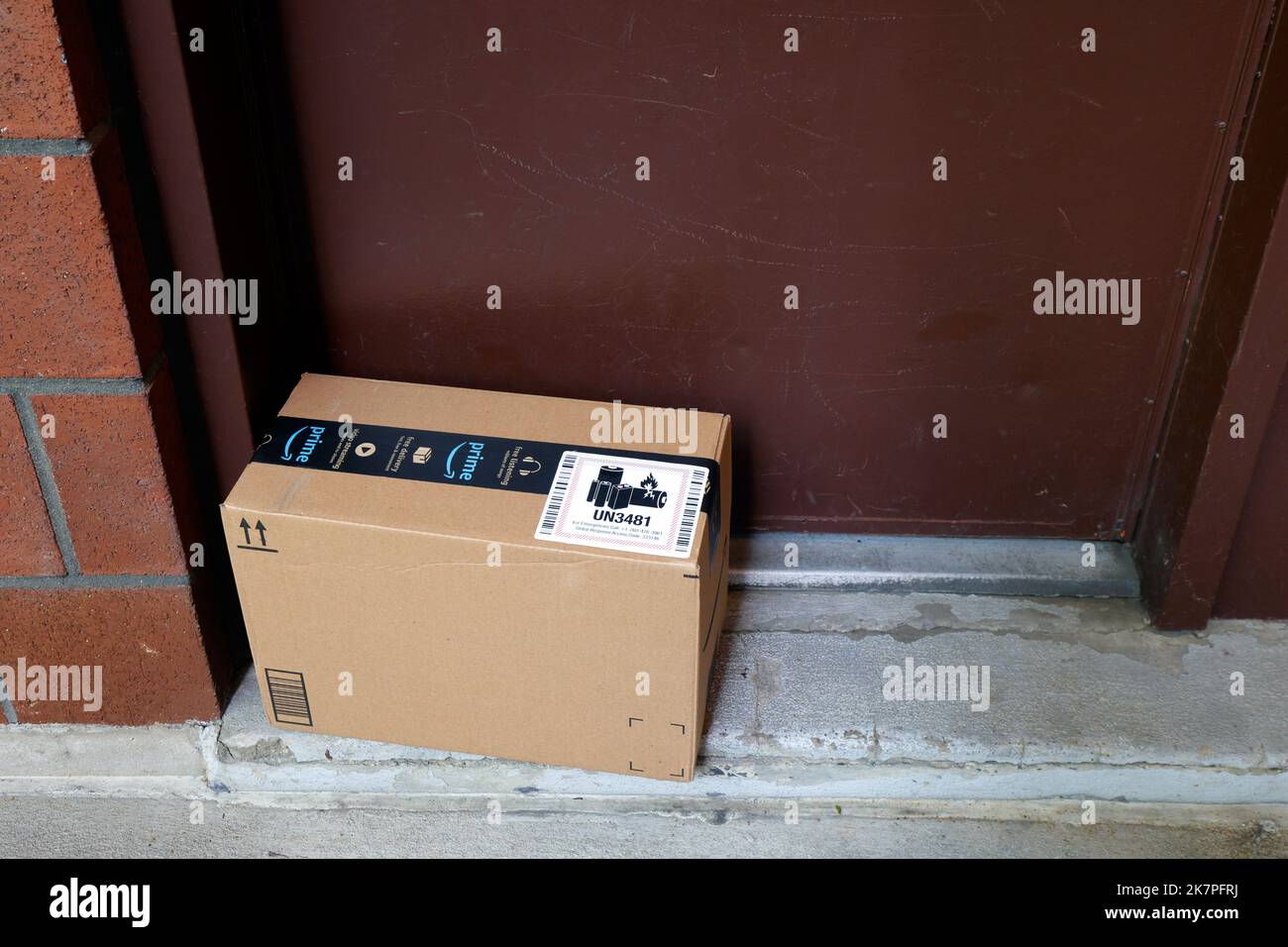 Una entrega de Amazon dejada en la puerta. Una pegatina UN 3481 en la caja de cartón que indica el contenido que contiene las baterías de iones de litio Foto de stock