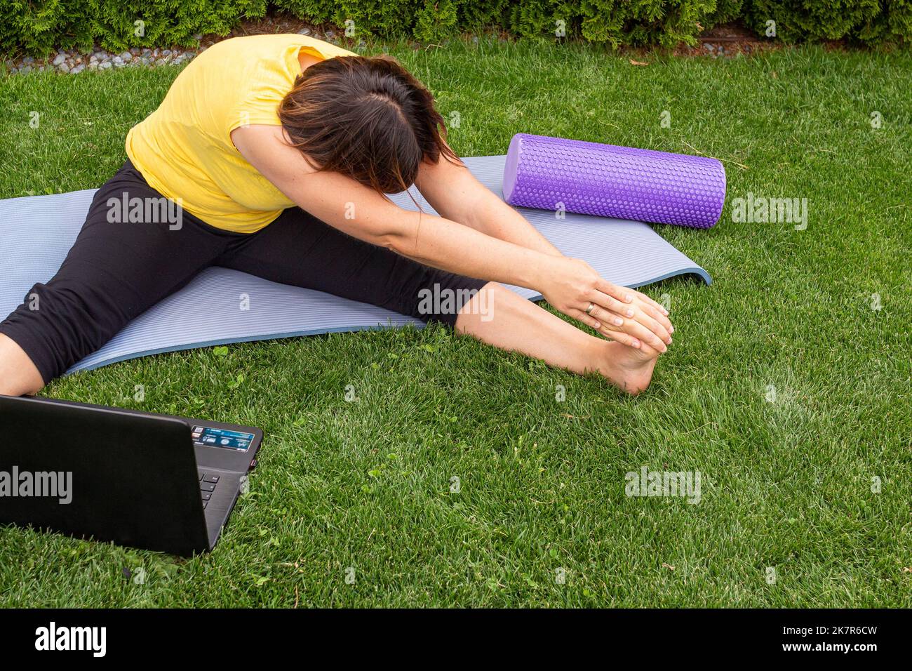 Mujer acostada en una colchoneta de yoga haciendo ejercicios de estiramiento Tomando una clase en línea en un prado en verano Foto de stock