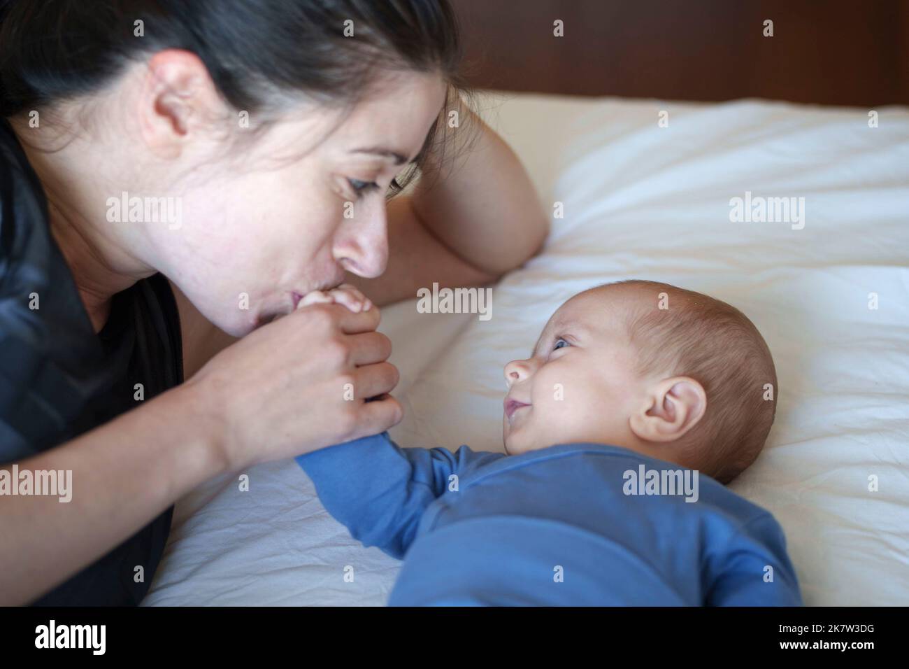 Cerca de la madre besando la mano de su bebé mientras él le sonríe Foto de stock