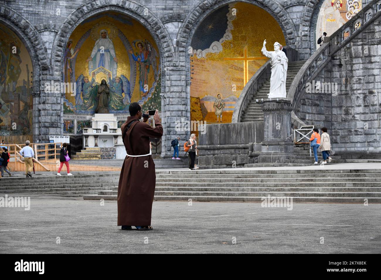 Lourdes, Hautes-Pyrénées, Francia, sacerdote religioso tomando una fotografía fuera de la catedral Foto de stock