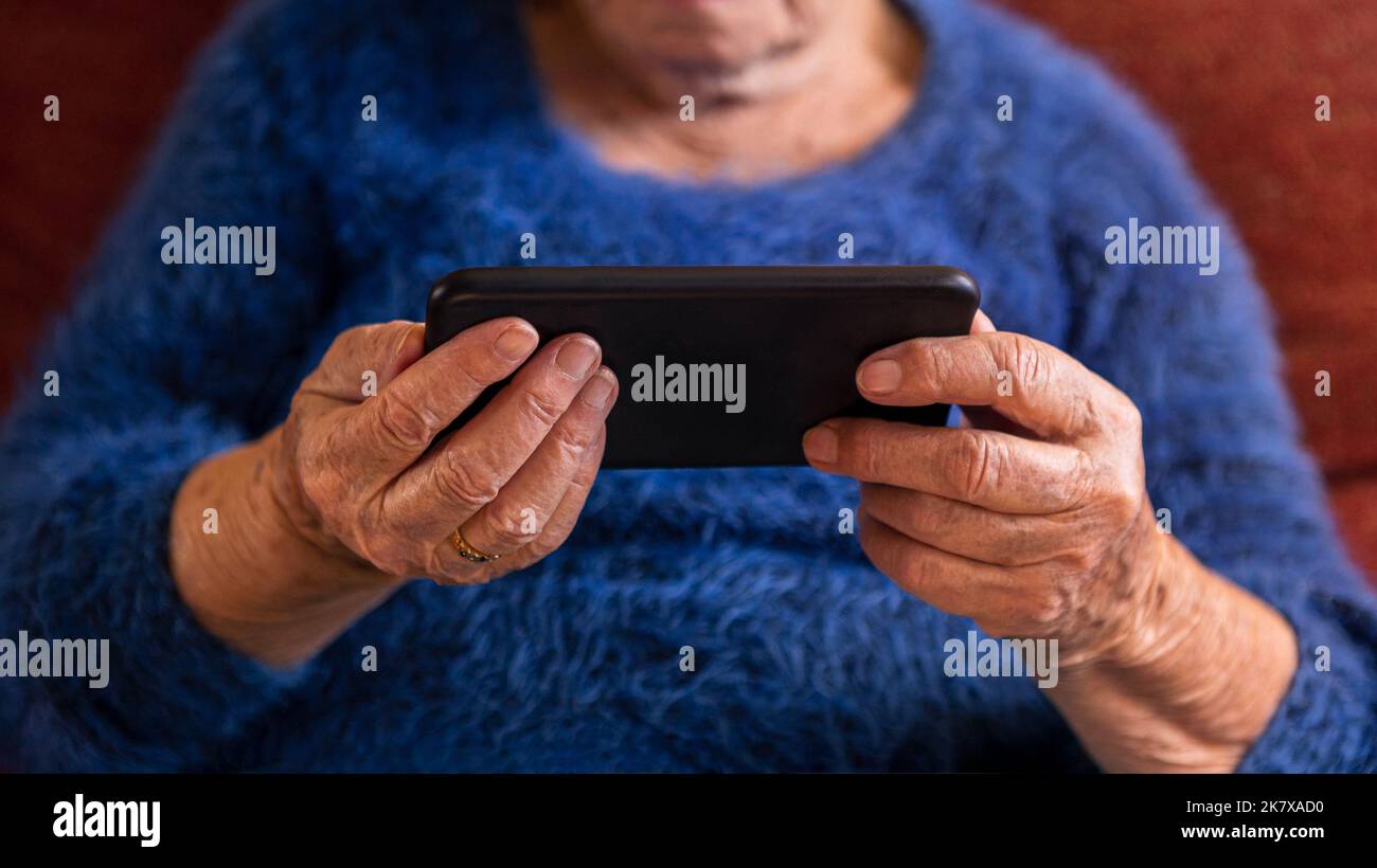 Las manos arrugadas de la anciana sostiene un smartphone. Primeros planos manos de abuela caucásica usando el teléfono para una nueva aplicación o sitio web. Foto de stock