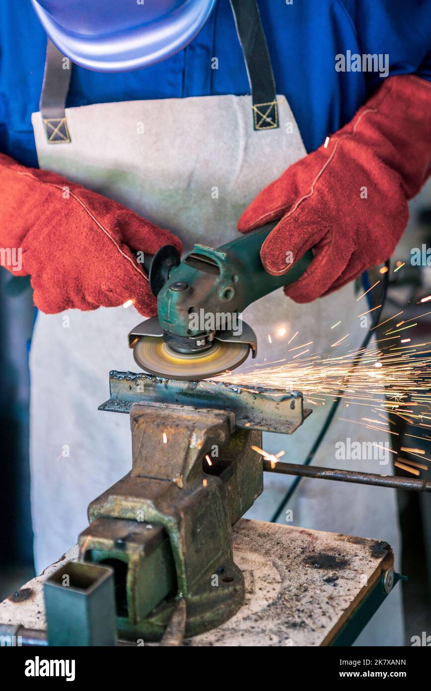 Trabajador que muele metal con una muela y que limpia la costura de acero. Trabajo en un taller de procesamiento de metales. El hombre trabaja con una herramienta eléctrica. Chispas Foto de stock