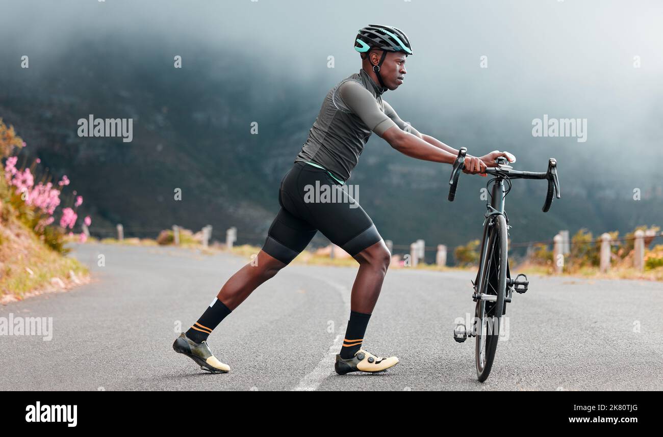 Estiramiento de piernas, fitness y hombre en bicicleta en una carretera con  una bicicleta en las montañas para cardio, viajes y ejercicios deportivos  en la naturaleza. Atleta haciendo un cálido Fotografía de