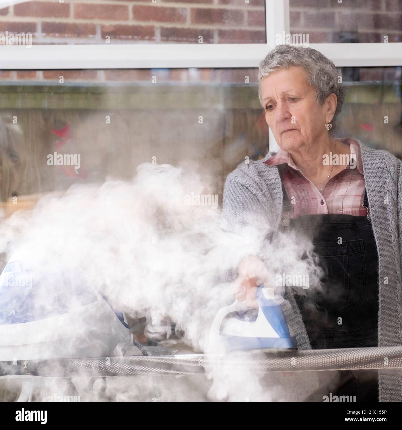 Una señora en casa haciendo el planchado en una nube de vapor Foto de stock