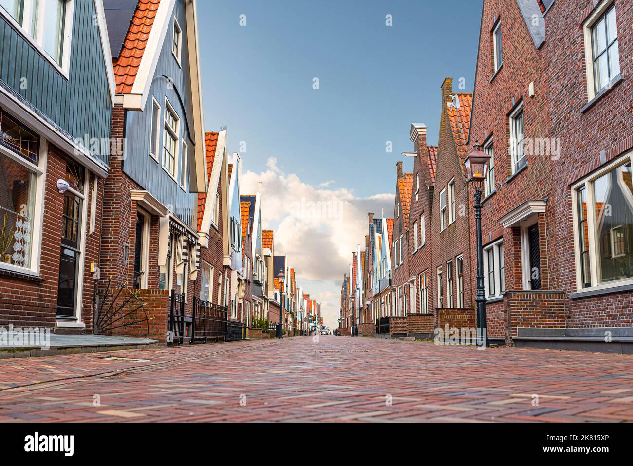 Vista de ángulo bajo de calles adoquinadas y edificios típicos en la ciudad holandesa de Volendam contra el cielo azul Foto de stock