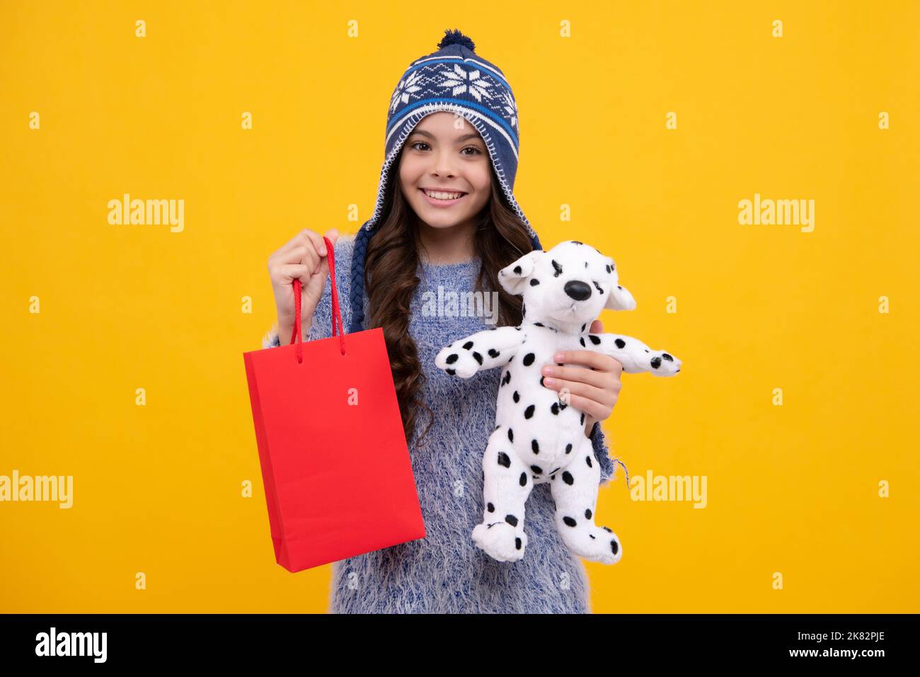 Hermosa moda adolescente niña en invierno cálido sombrero con bolsas de compras sobre fondo amarillo. Compras y moda. Niño con compras Foto de stock