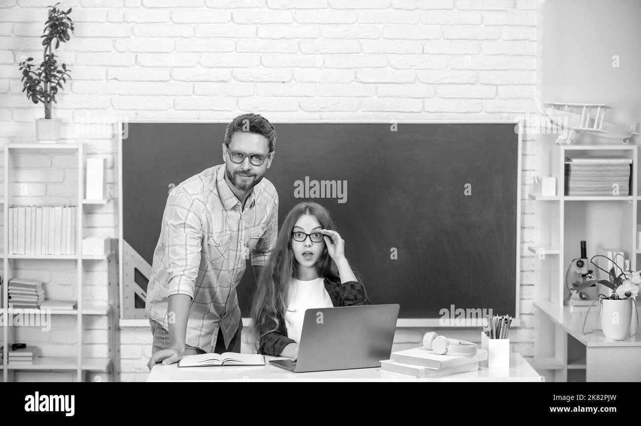 asombrado padre y niño estudio en la escuela con ordenador portátil sobre fondo de pizarra, e-learning Foto de stock