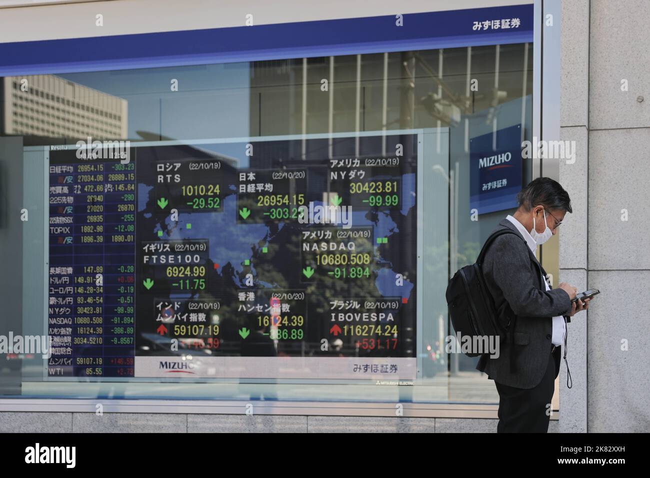 Tokio, Japón. 20th de Oct de 2022. Un hombre mira su teléfono mientras se  encuentra cerca de una placa electrónica que muestra datos económicos en tiempo  real. El yen continuamente débil ha