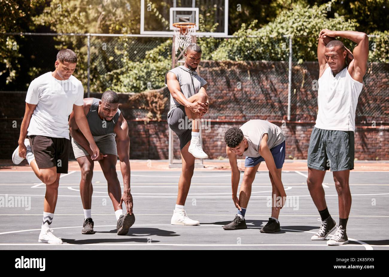 Hombres de fitness, ejercicio y baloncesto estirando o entrenando su cuerpo  en una cancha deportiva. Los atletas masculinos de entrenamiento preparan  el calentamiento muscular antes de la práctica Fotografía de stock -