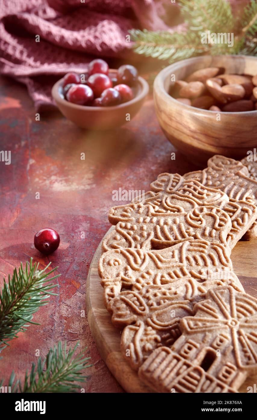 Speculoos o Spekulatius, galletas de Navidad, con bayas de arándano rojo, almendras sobre una mesa con toalla textil y ramitas de abeto. Dulces alemanes tradicionales Foto de stock