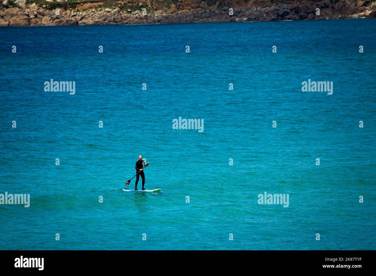 Un paddleboarder parado en el mar azul Foto de stock