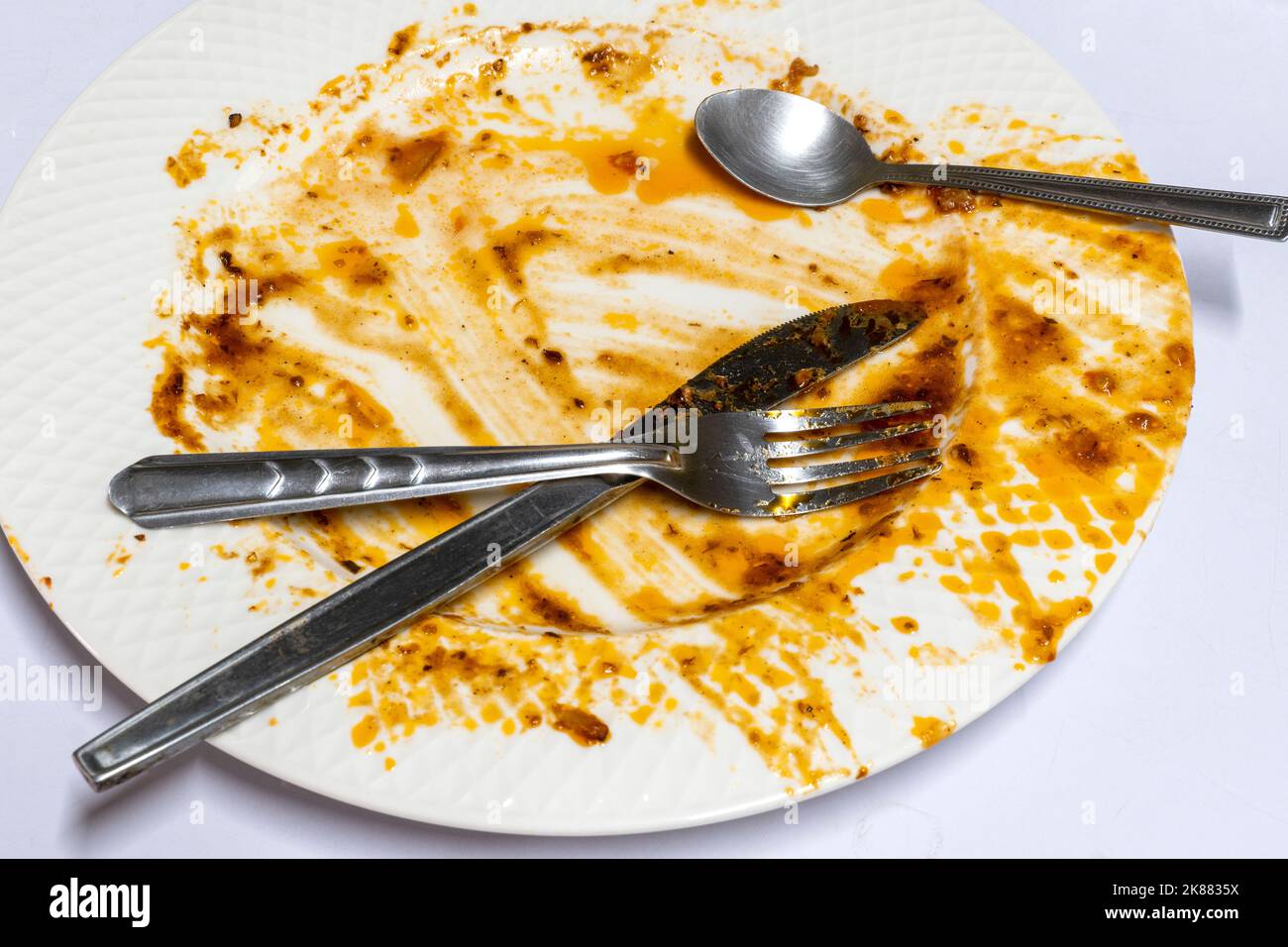 Plato llano sucio y vacío con tenedor y cuchara sobre mesa blanca en la cocina. Foto de stock