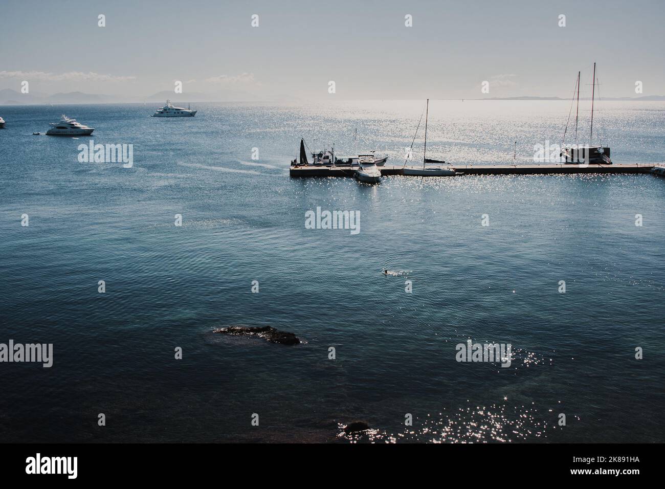vista del muelle de yates del paseo marítimo de madera en aguas azules que reflejan la luz del sol en grecia Foto de stock