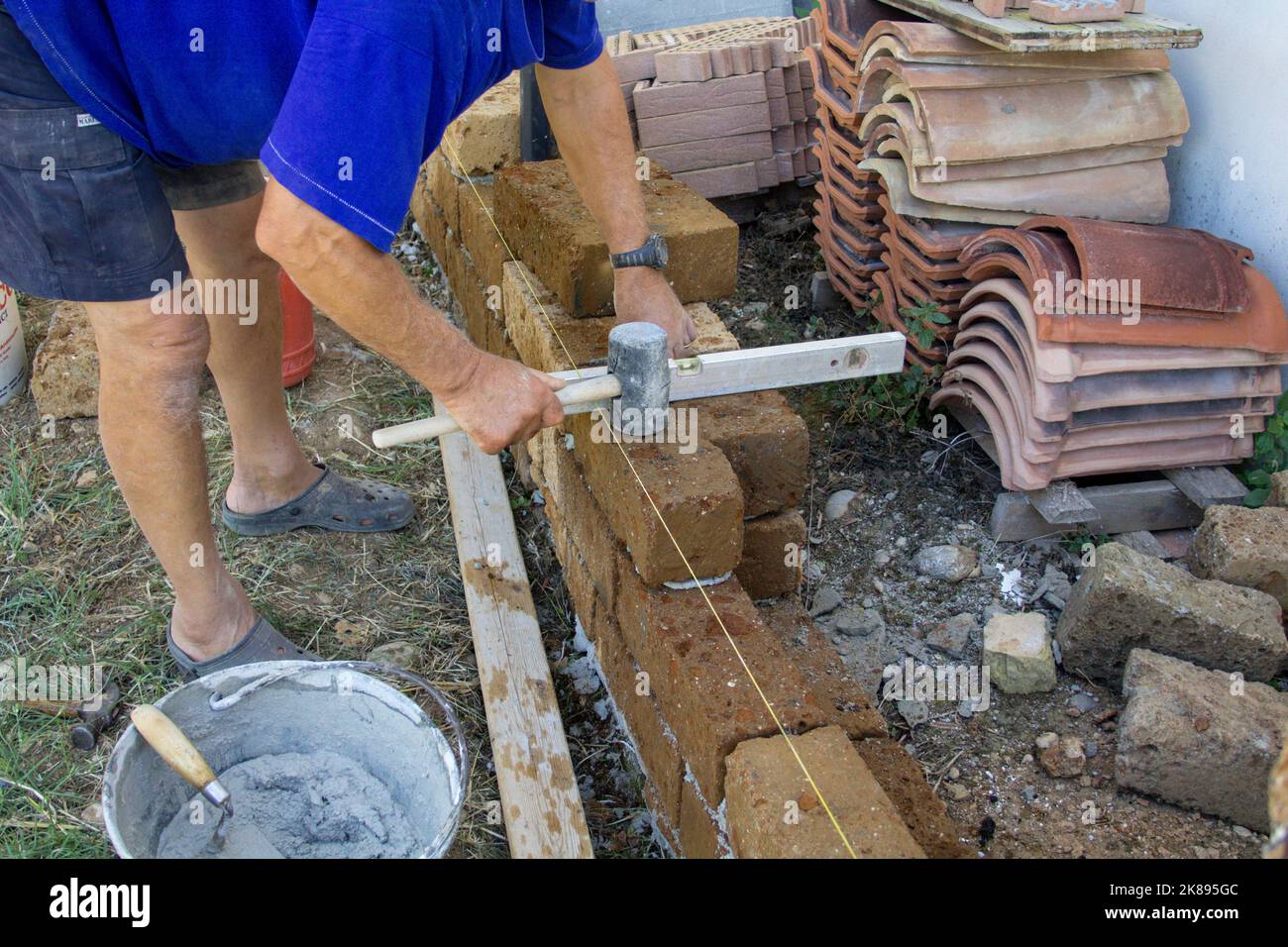 Imágenes de las manos de un viejo albañil mientras con cemento construye una pared baja con ladrillos de toba. Hombre en el trabajo Foto de stock