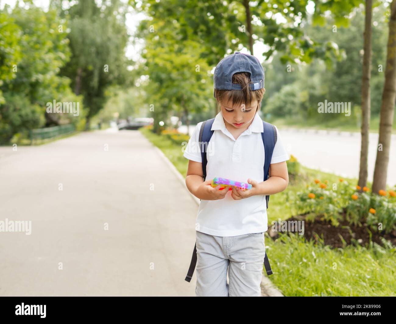 El niño pequeño juega el juguete cuadrado del fidget de caucho Pop él. Juguete táctil y antiestrés de color arco iris para todas las edades. Recreación al aire libre con juguete para motor fino Foto de stock