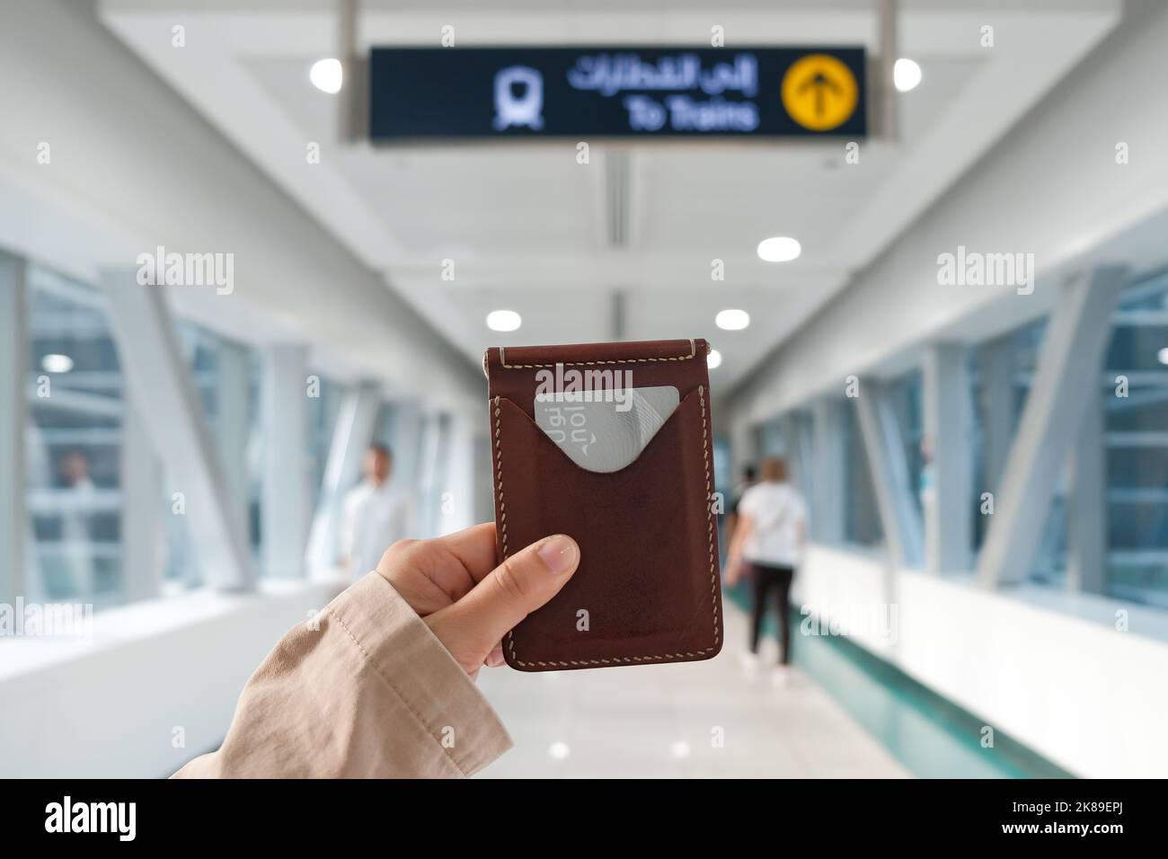 La mano hembra sostiene el portador de la tarjeta de cuero con la tarjeta azul del metro de Dubai de plata en una estación de tren en la ciudad moderna del Oriente Medio. Tarifa electrónica sin contacto. Foto de stock