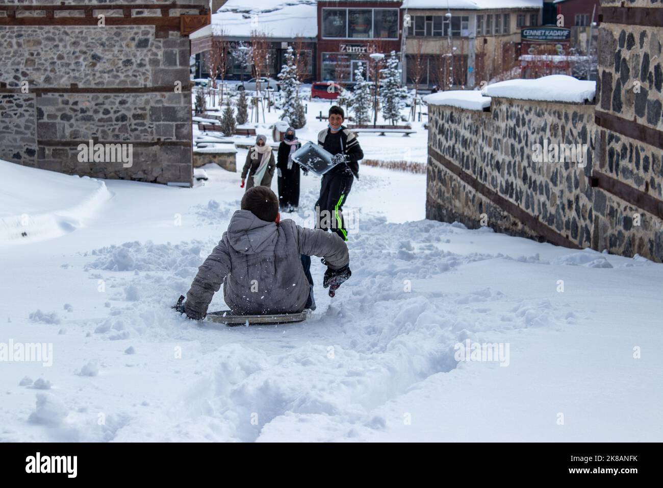 Erzurum, Turquía - Enero 2021 Los niños se deslizan cuesta abajo en la nieve en las calles históricas de Erzurum. Foto de stock