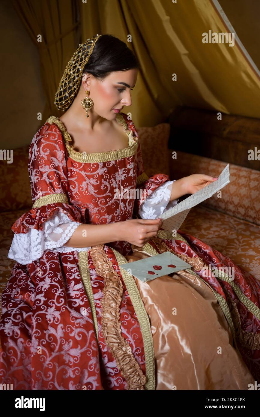 Dama renacentista en vestido medieval tardío sentado en una hermosa cama con dosel en su dormitorio del castillo Foto de stock