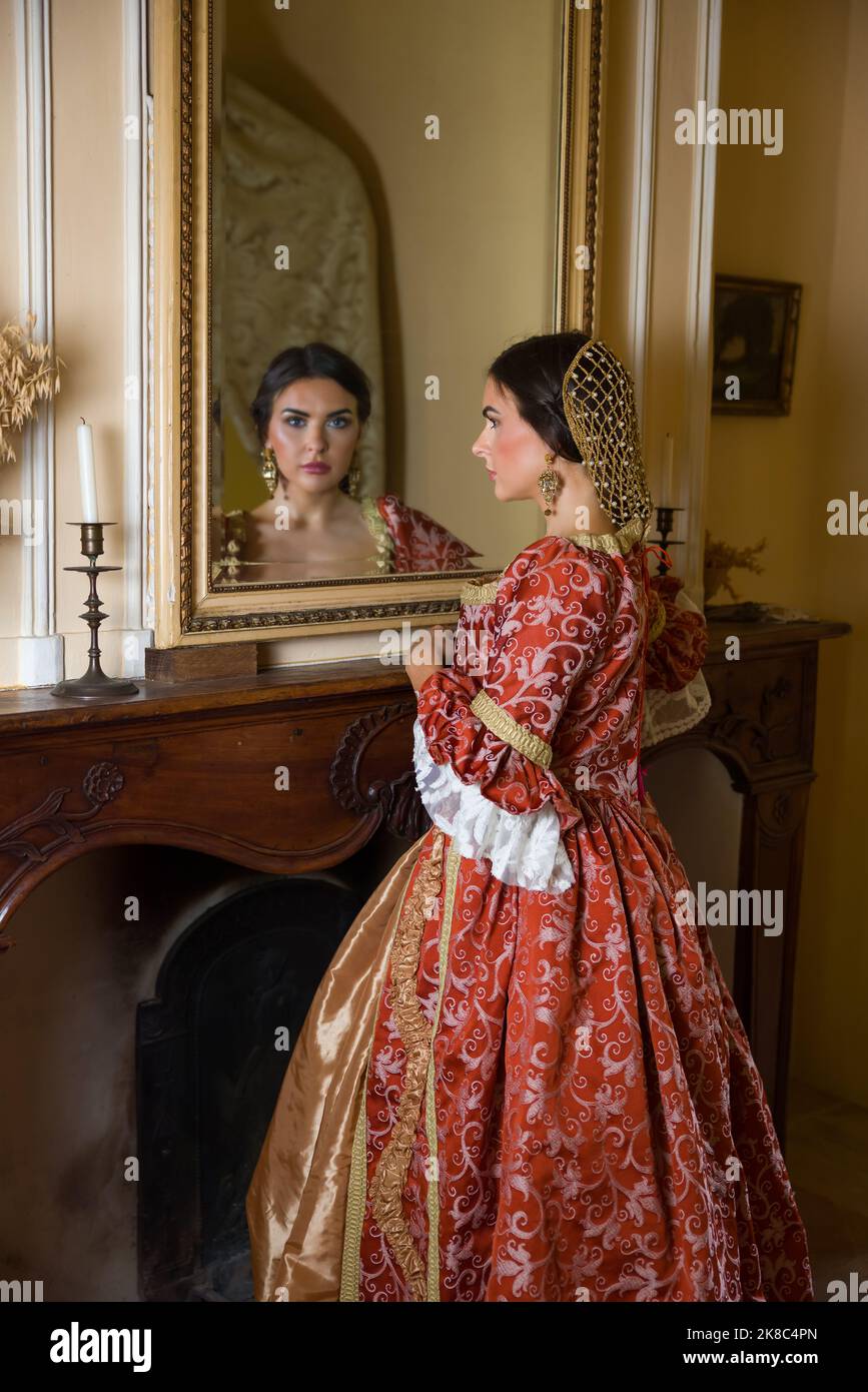 Hermosa mujer en vestido renacentista mirando en un antiguo espejo dorado en su castillo Foto de stock
