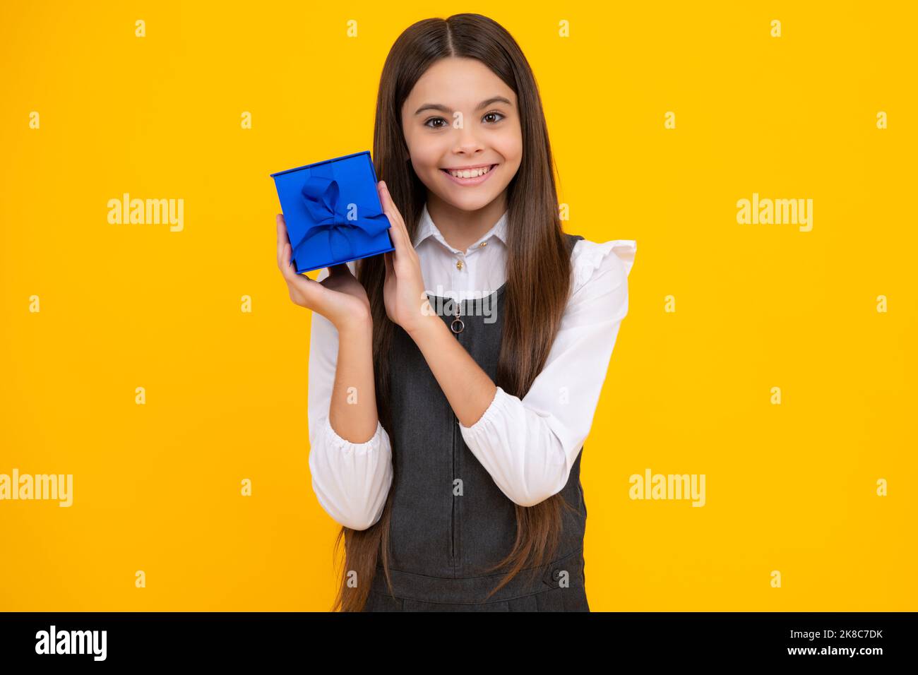 Retrato de una niña adolescente que sostiene la caja presente aislada sobre el fondo amarillo del estudio. Concepto de regalo, saludo y regalo. Vacaciones de cumpleaños Foto de stock