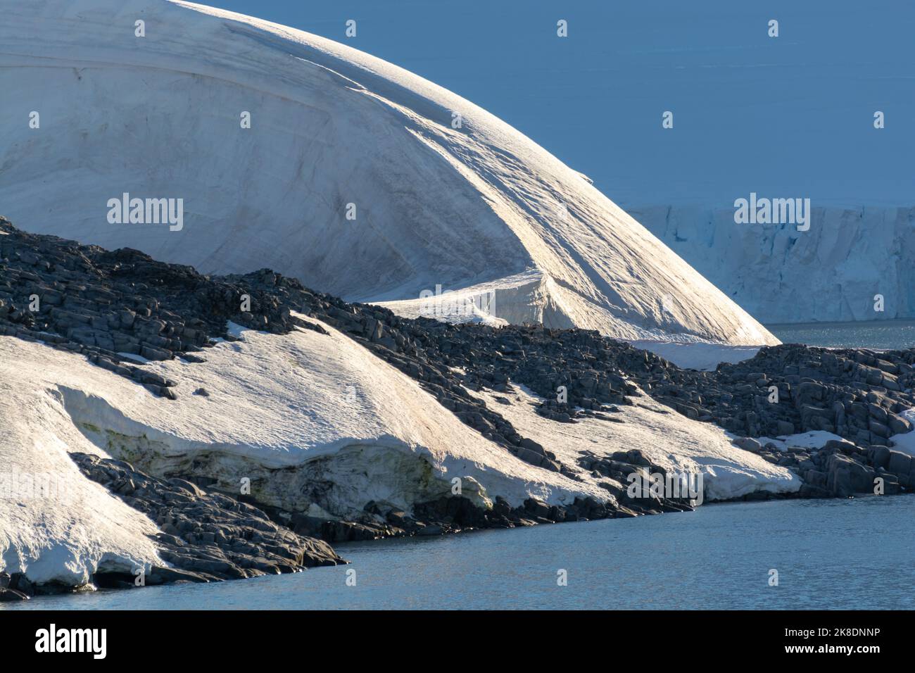 detalle de hielo, nieve y roca de la isla wiencke en la costa del puerto lockroy con picos nevados de la isla anvers detrás. península antártica Foto de stock