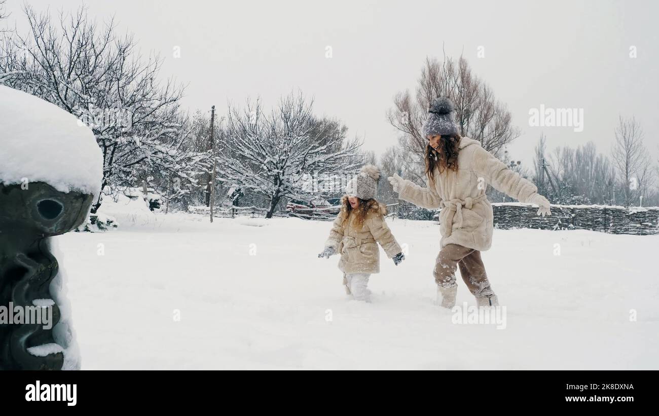 actividad familiar de invierno al aire libre. vista lateral. Chicas felices, los niños caminan lentamente a través de la nieve espesa en el parque de la ciudad, durante la nevada. La familia se divierte, pasando tiempo juntos en el día nevado del invierno. Cámara lenta. Fotografía de alta calidad Foto de stock