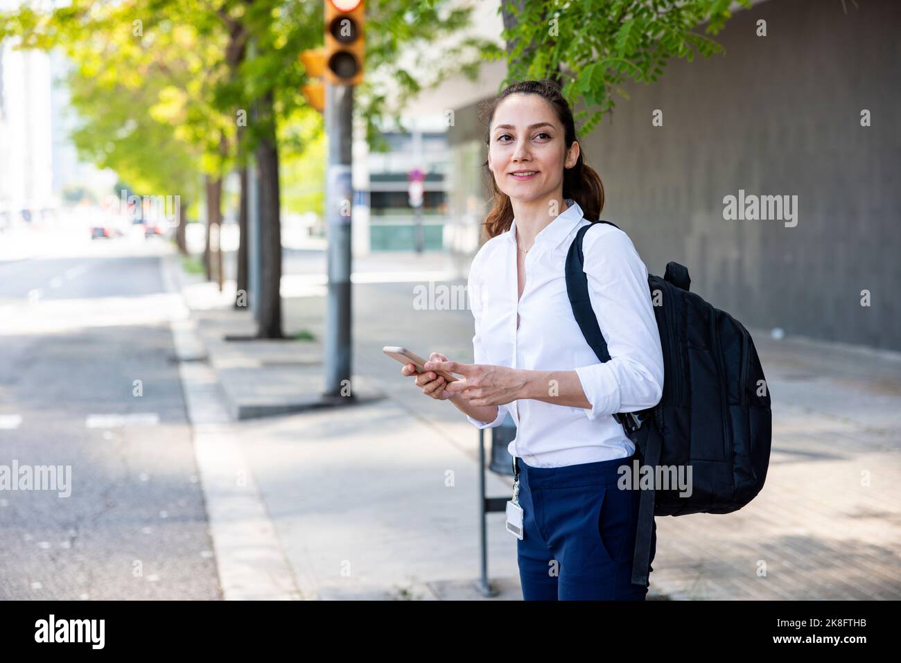 Mujer de negocios feliz con el teléfono inteligente y la mochila de pie en  el sendero Fotografía de stock - Alamy