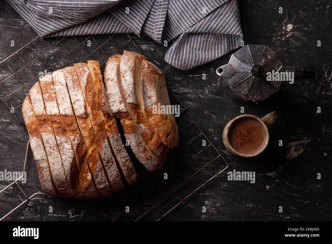 Pan redondo de masa madre recién horneada con una cafetera y una taza de café y una servilleta sobre un fondo oscuro. Foto de stock