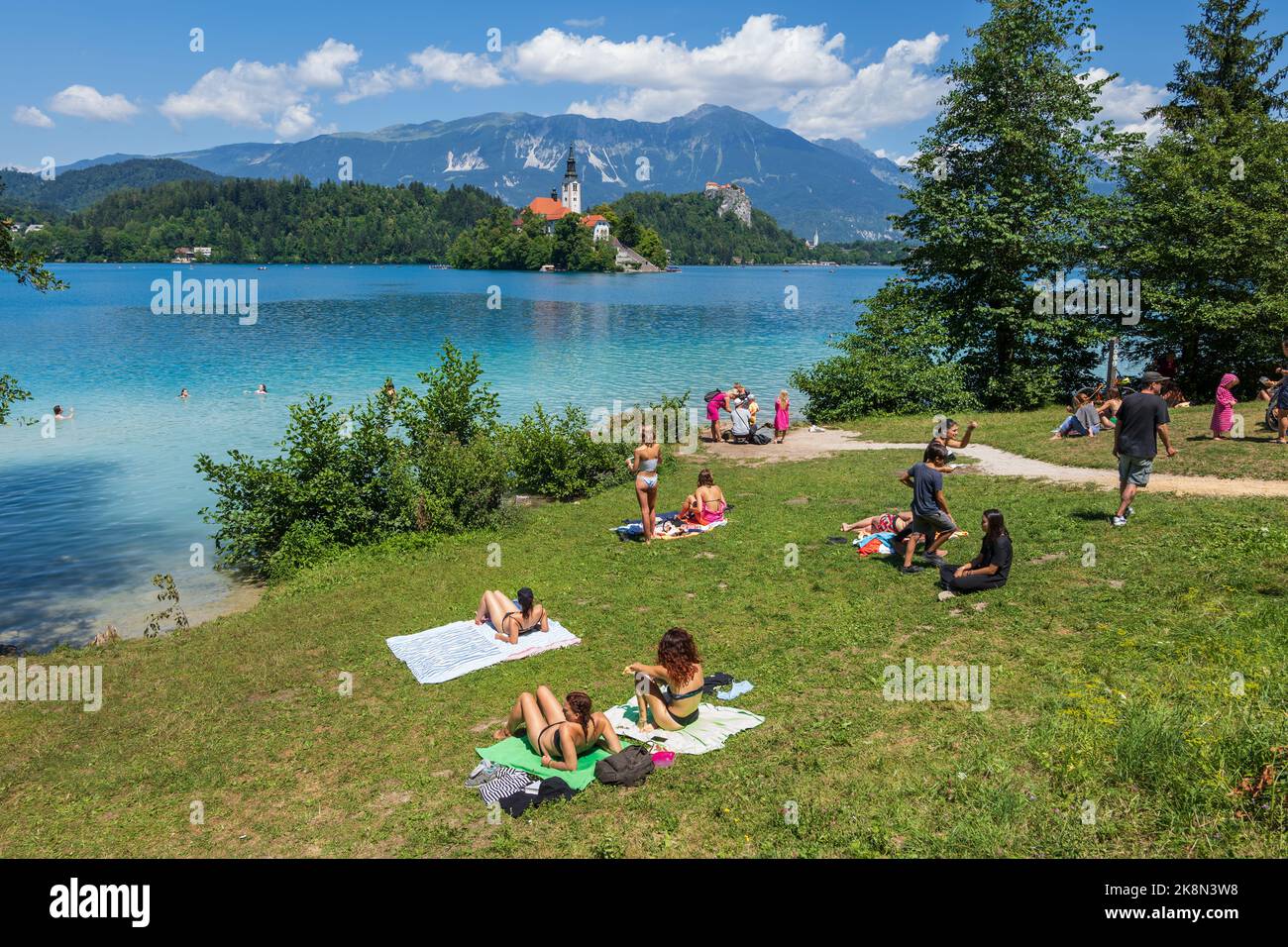 Bled, Eslovenia - 18 de julio de 2022: La gente se relaja en el lago Bled en el verano, nadar y tomar el sol en la costa con vistas a la isla de Bled, lugar de interés natural y. Foto de stock