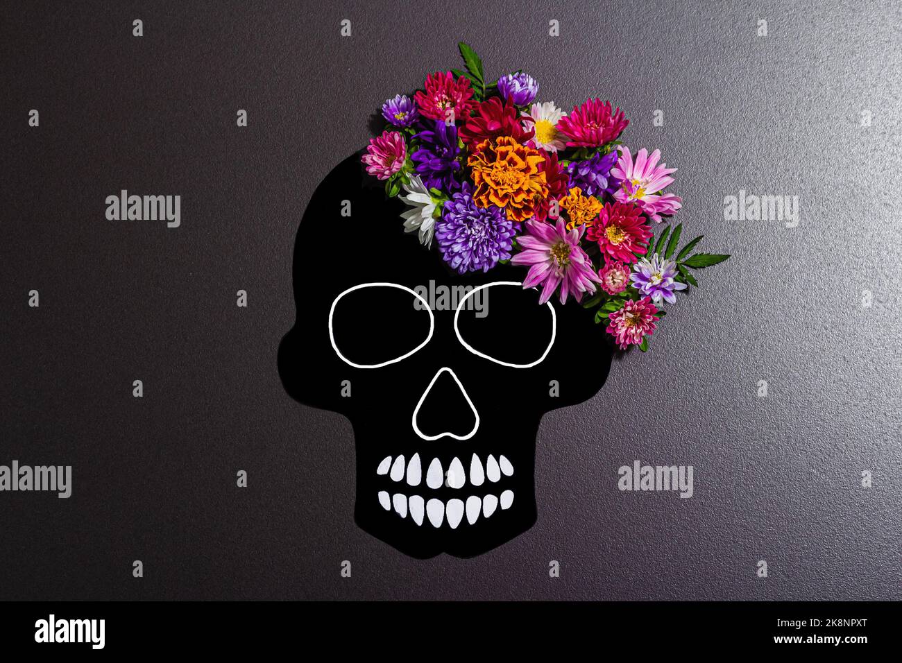 Cráneo humano de papel para el Día de Muertos de México (El Dia de Muertos)  con flores tradicionales. Moderna luz dura, sombra oscura. Fondo de  hormigón de piedra negra Fotografía de stock -
