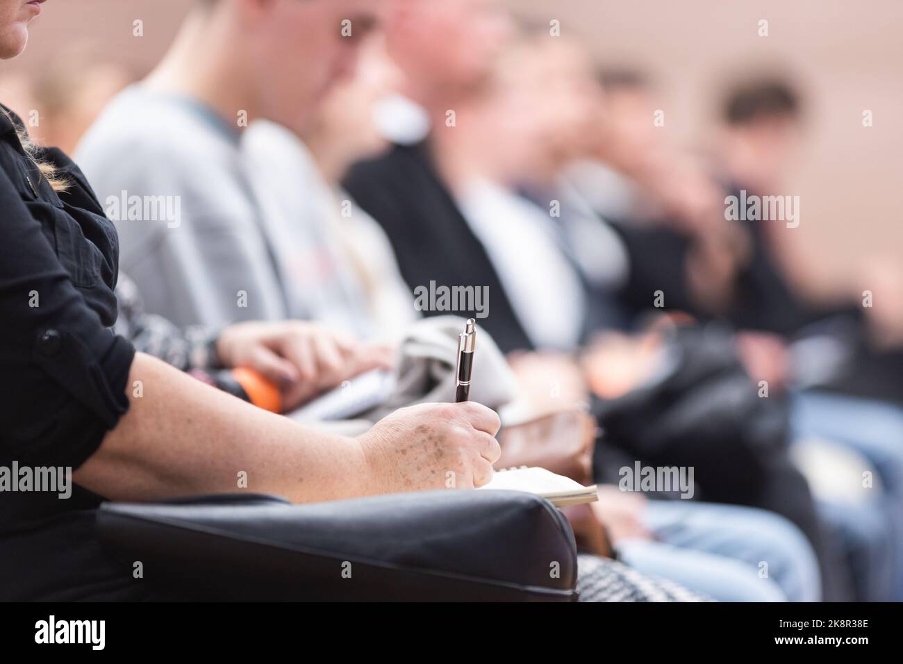 Mujer con las manos sujetando el bolígrafo y el cuaderno, tomando notas en una conferencia. Participantes del evento en la sala de conferencias. Foto de stock