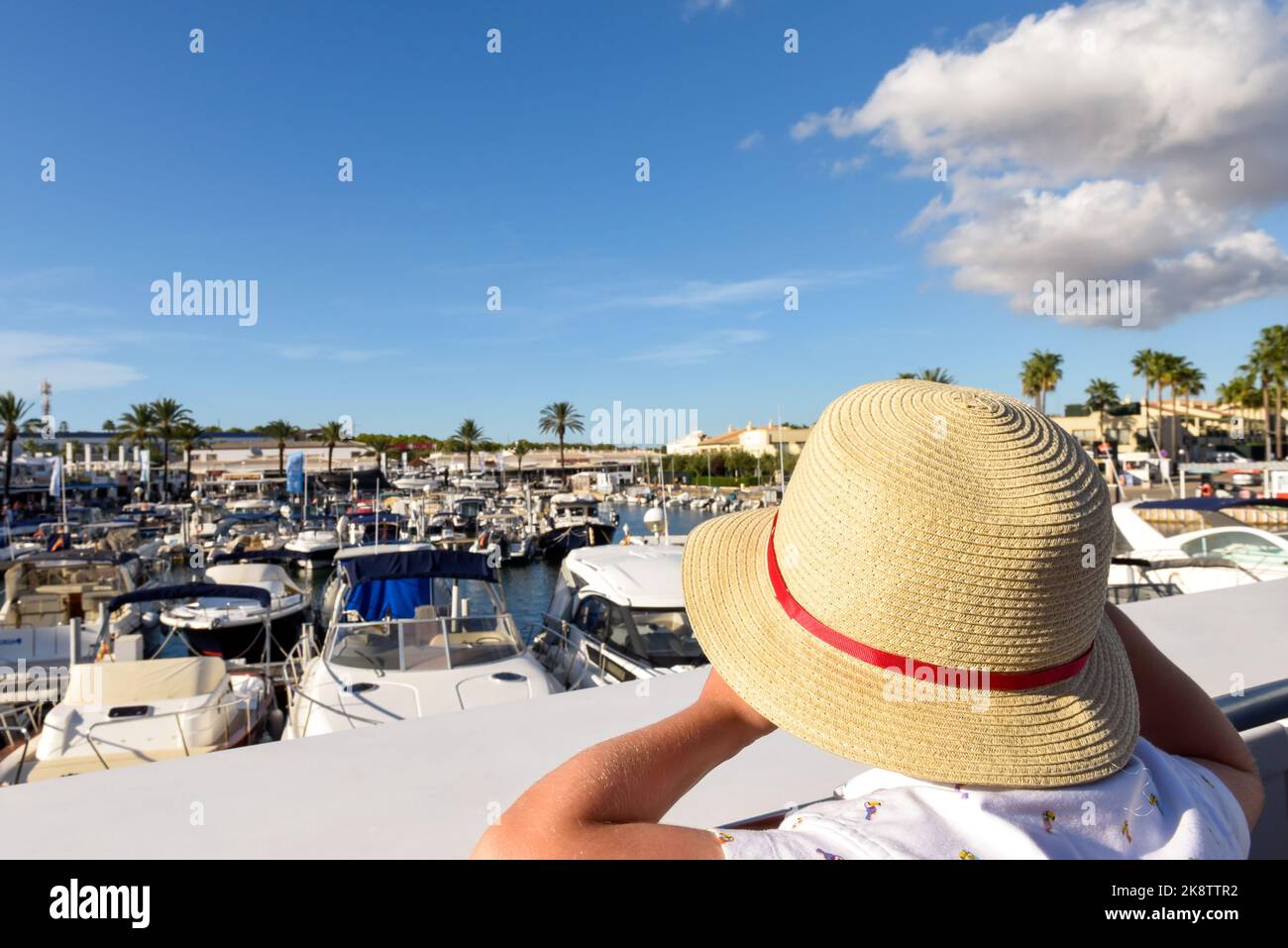 Niño pequeño mirando por encima de un puerto deportivo usando un sombrero para el sol Foto de stock