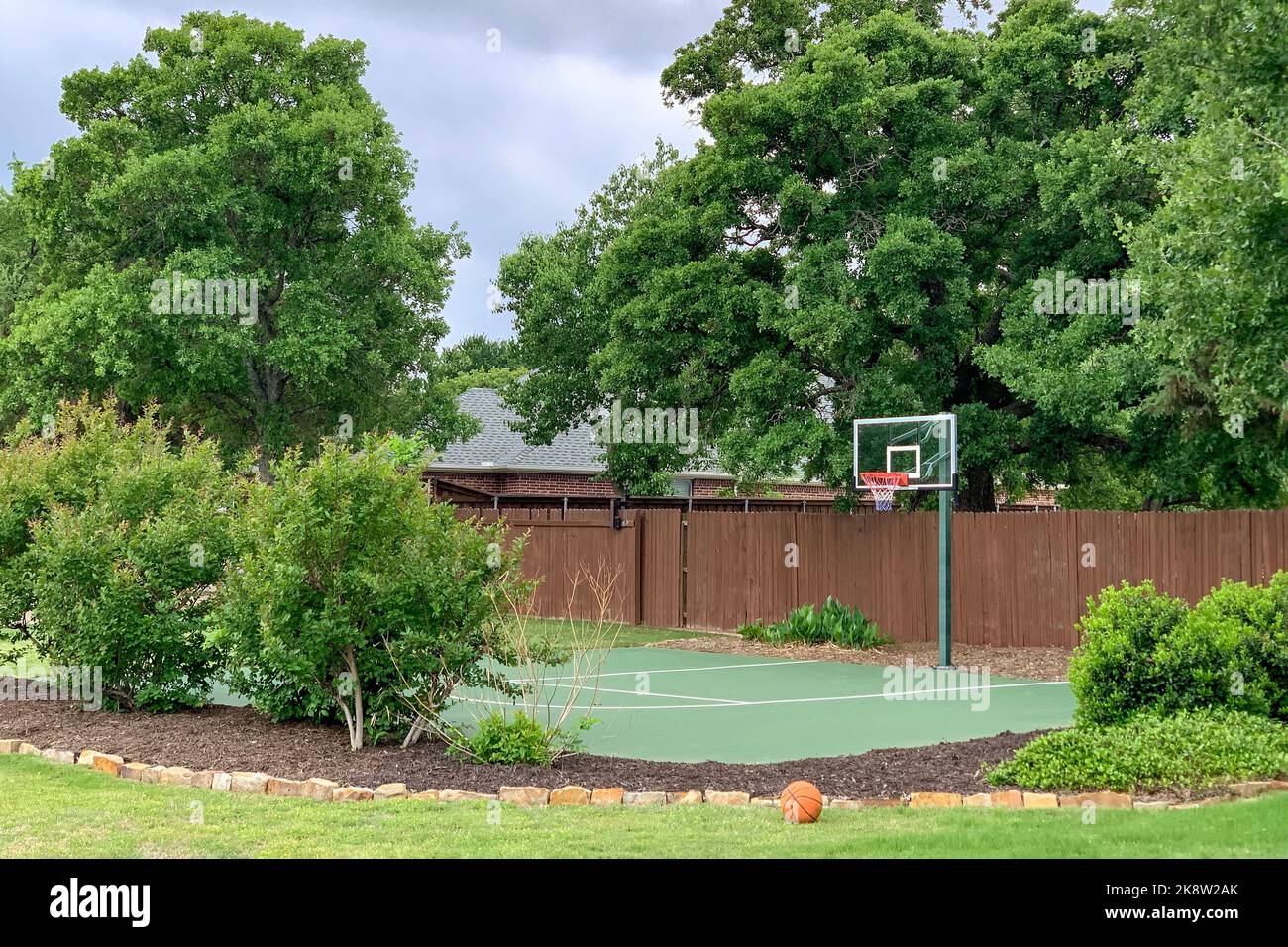 Tiro al aire libre de patio trasero de la casa de campo en los suburbios con árboles, arbustos, flores y cancha de baloncesto, zona de actividad en el hogar. Foto de stock