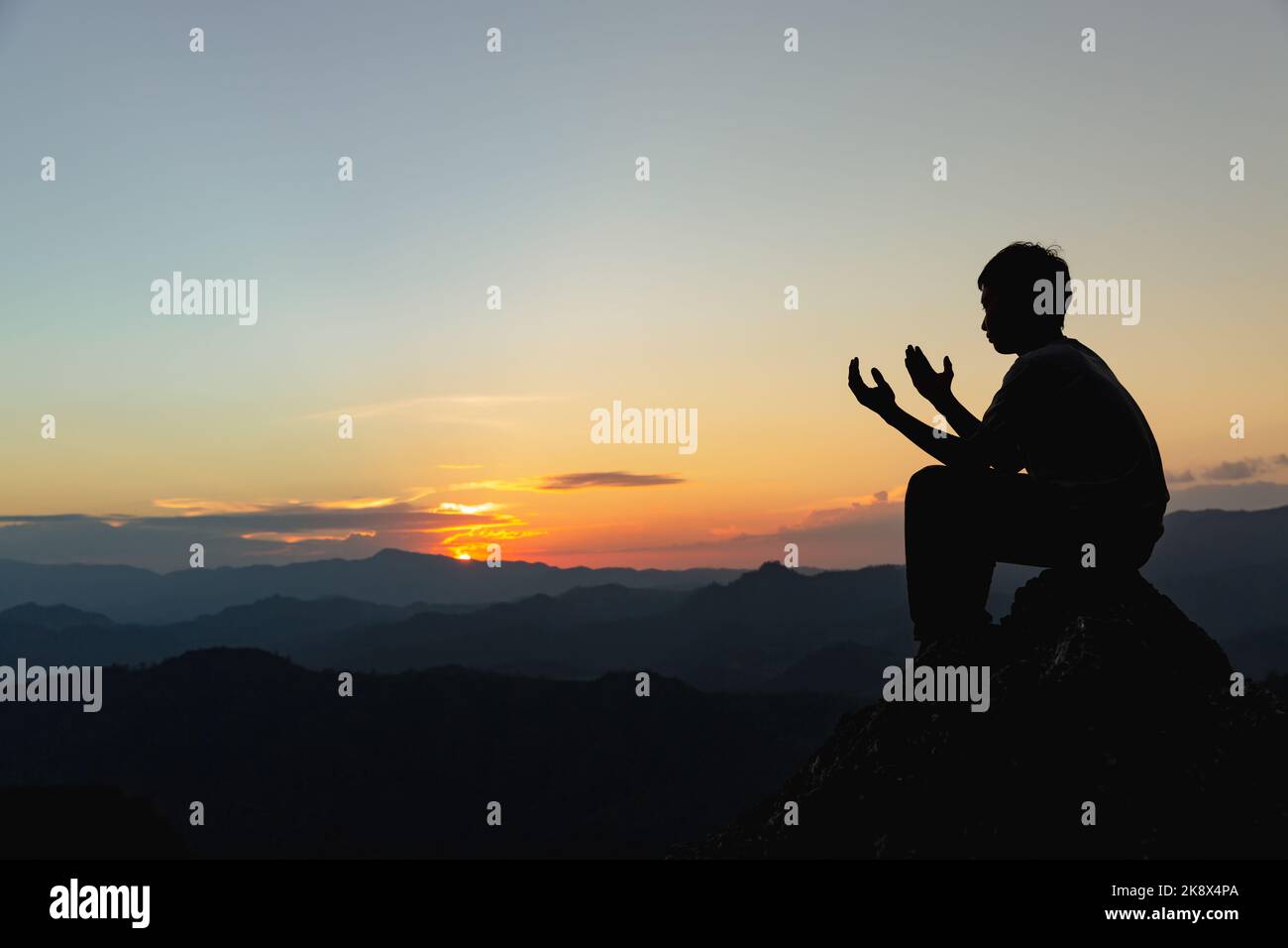 Silueta de un joven rezando a Dios en la montaña al atardecer. Mujer