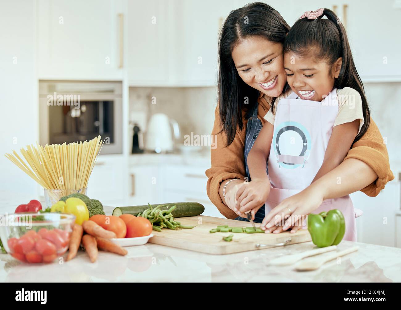 Feliz, madre y niño aprendiendo a cocinar con una sonrisa para ayuda, orientación y apoyo en la cocina. Mamá ayudando a su niña corta verduras, comida Foto de stock