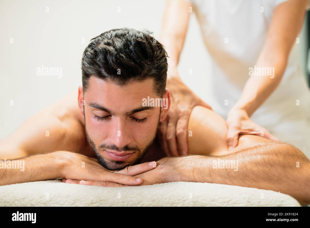 Un hombre barbudo guapo del salón de masajes tumbado en la mesa y recibiendo un masaje de espalda en el spa del complejo Foto de stock