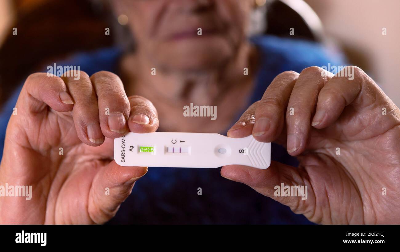 Una abuela caucásica triste hace un dispositivo de prueba rápida para el virus Covid19 con un resultado positivo. Abuela infeliz utilizando un casete de antígeno de pcr Foto de stock
