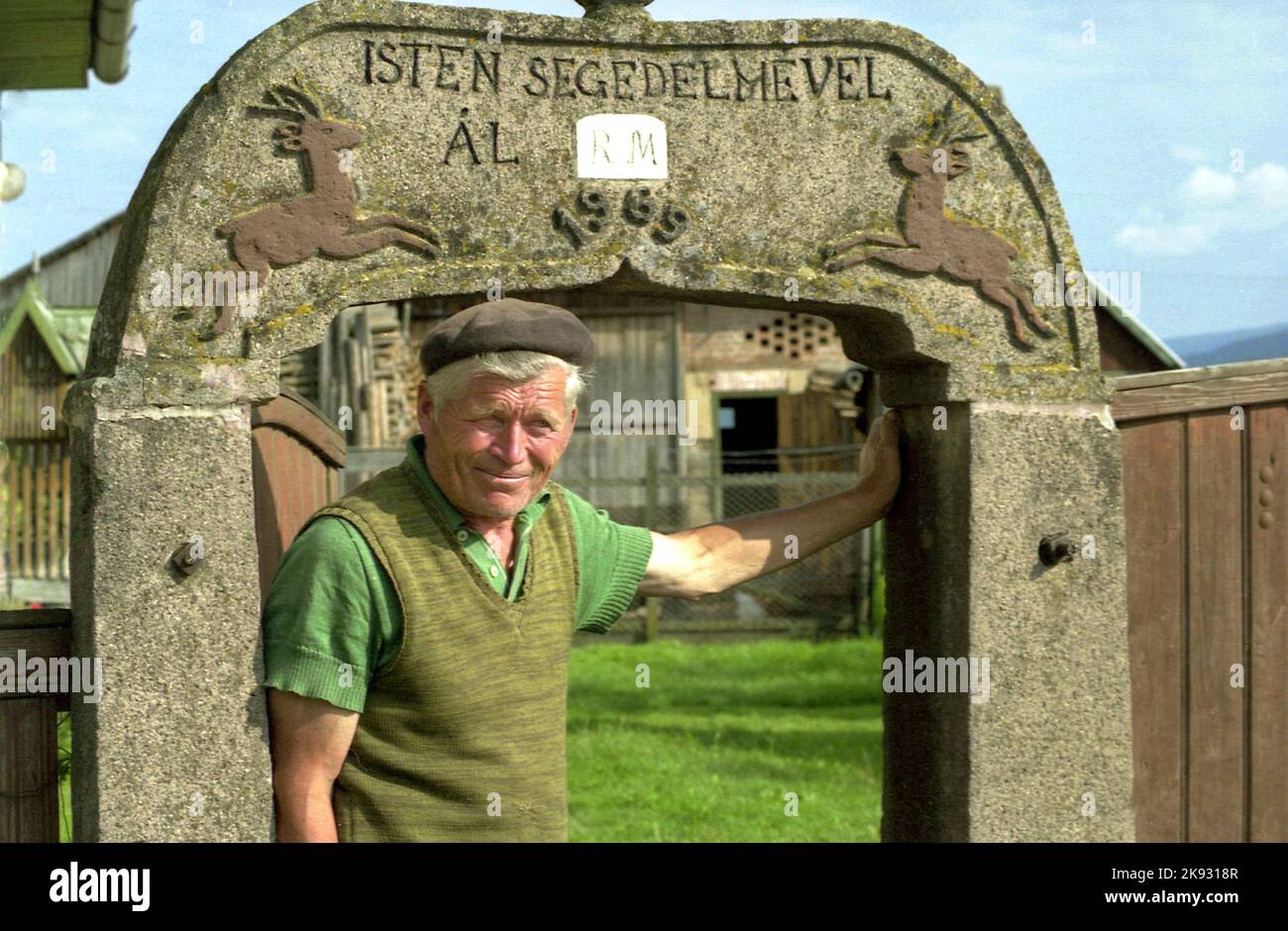 Condado de Harghita, Rumania, 2003. Hombre local parado junto a su puerta de piedra única, con la inscripción tallada 'Isten segedelmével (con la ayuda de Dios), 1969'. Foto de stock