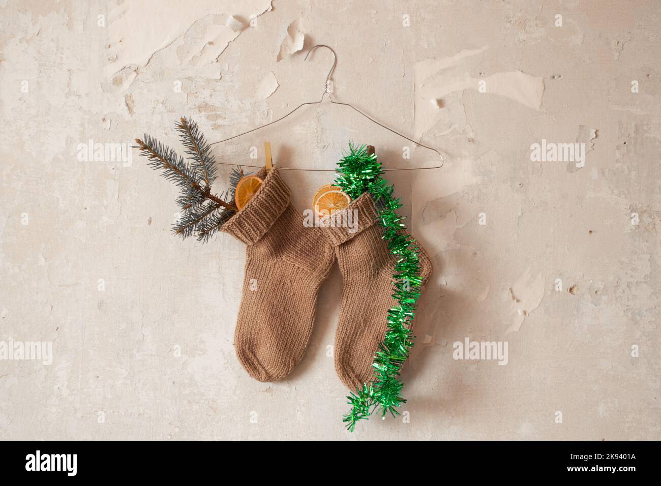 Calcetines de punto con una rama de Año Nuevo y una naranja seca y una guirnalda cuelgan en perchas en la pared, regalos de Año Nuevo en calcetines Foto de stock
