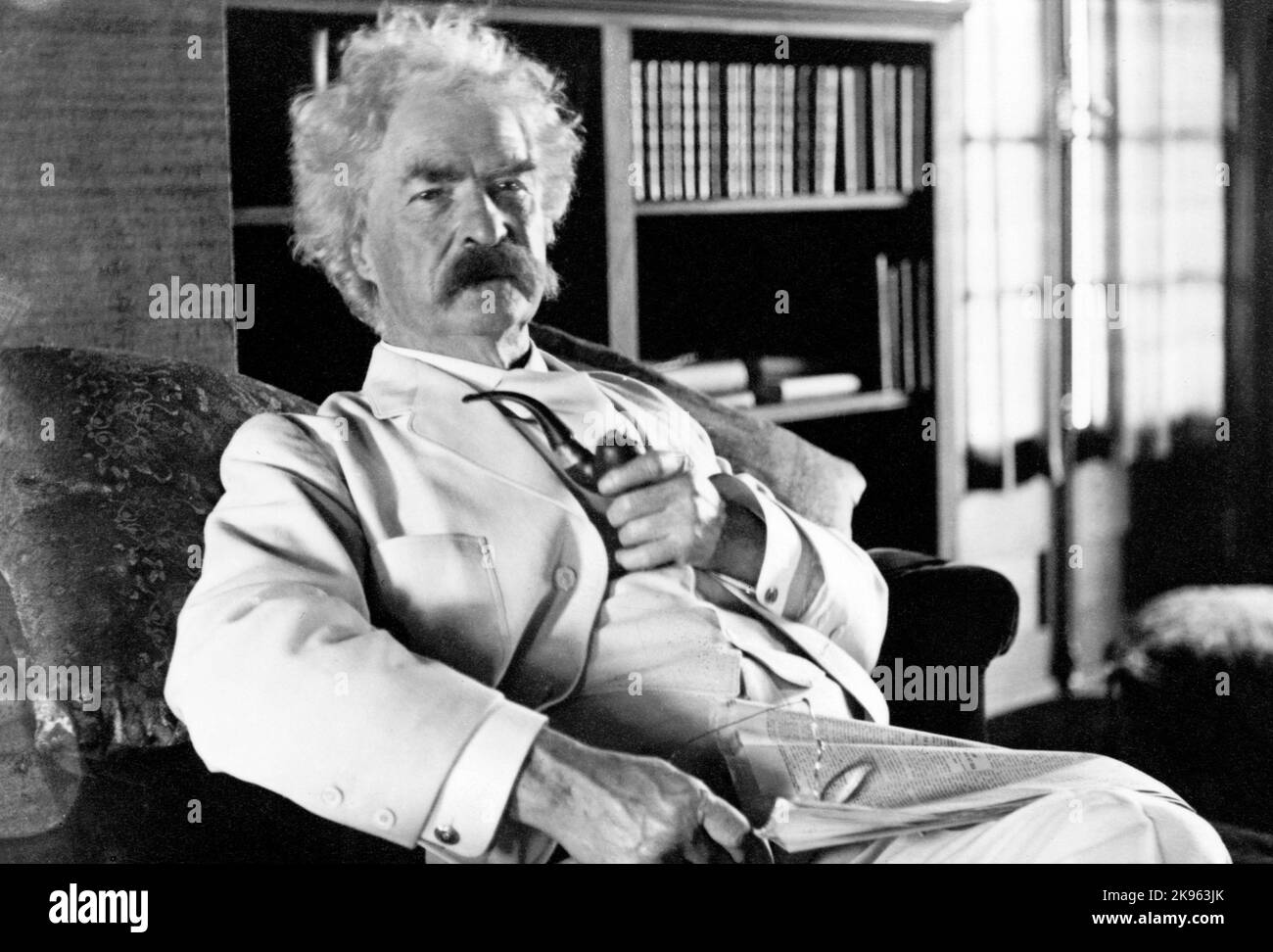 Mark Twain (Samuel L. Clemens) Retrato de tres cuartos de longitud, sentado, mirando ligeramente a la derecha, sosteniendo la pipa Foto de stock