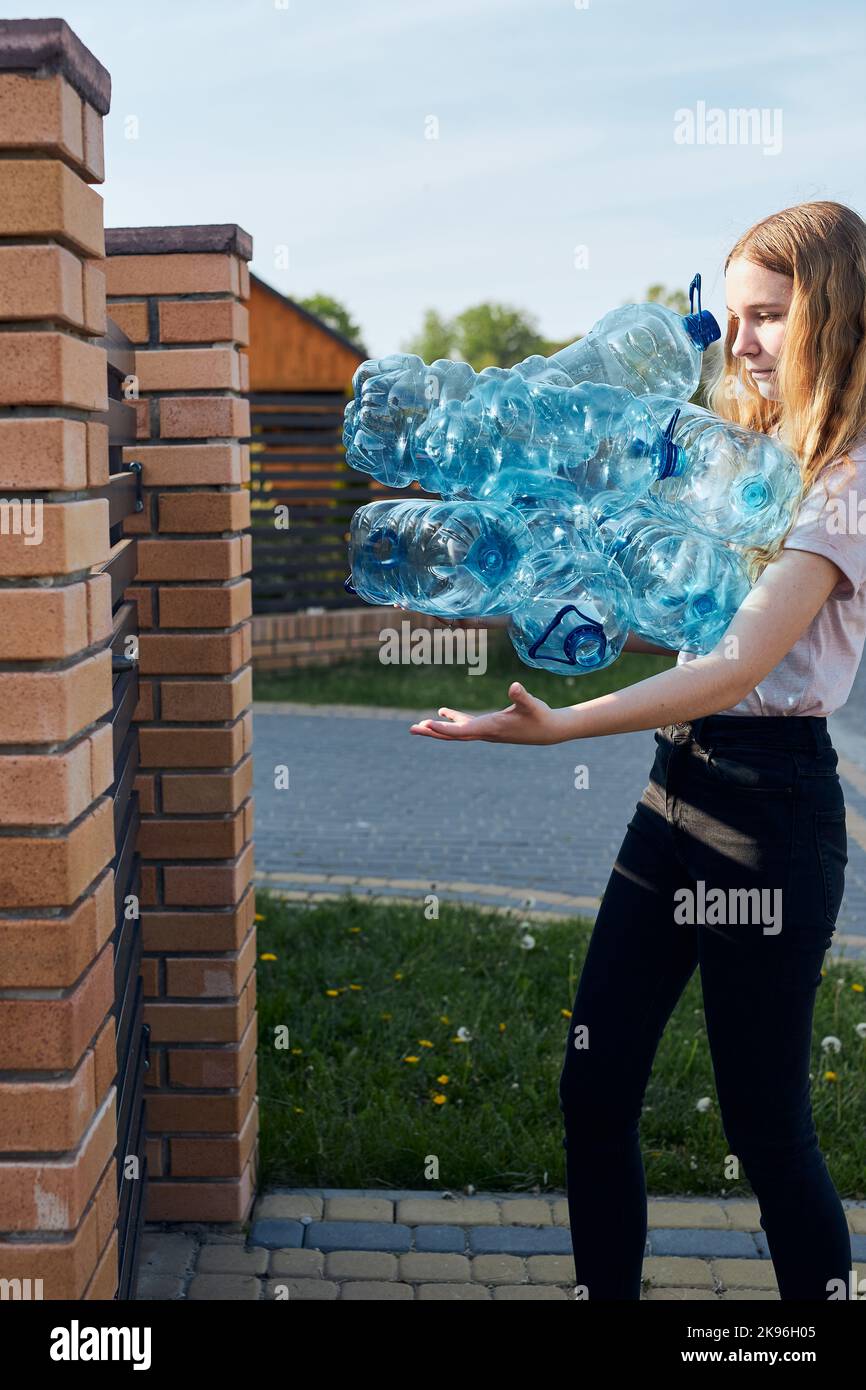 Mujer joven arrojando botellas de plástico vacías de agua en un cubo de basura. Recogida de residuos plásticos para reciclaje. Concepto de contaminación plástica y también Foto de stock
