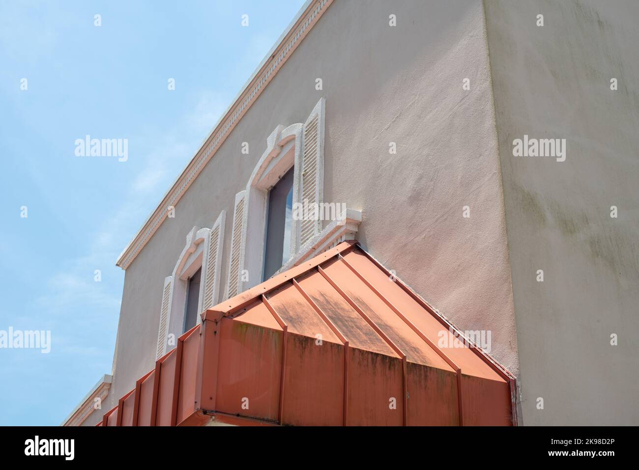 Renderizado en el exterior de un edificio histórico con dos ventanas. Hay una gruesa moldura blanca y persianas en la pared exterior y una sombra de cobre. Foto de stock