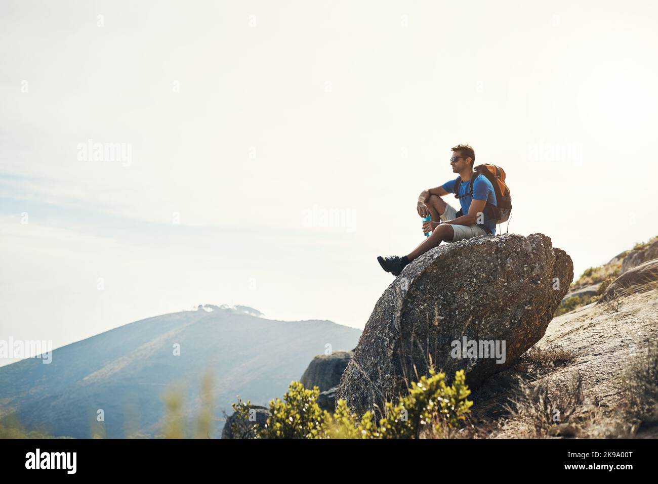 Puedo quedarme aquí para siempre. Un joven despreocupado sentado en la cima de una montaña después de un día de senderismo. Foto de stock