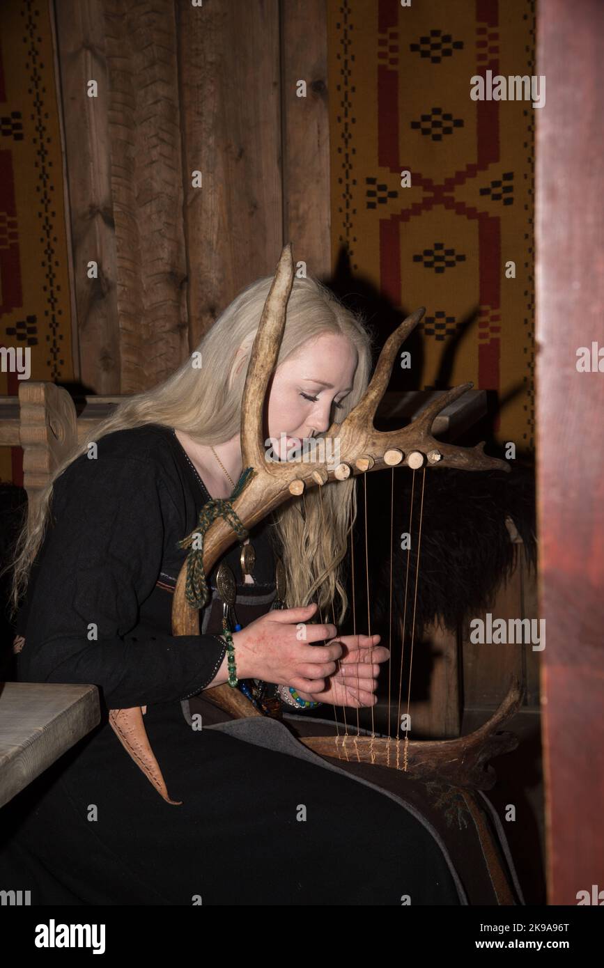 Actriz vikingo interpretando un instrumento de cuerda como arpa en un local  de un cacique vikingo en Borg, en la isla de Vestvågøya, en el archipiélago  de Lofoten en Noruega Fotografía de