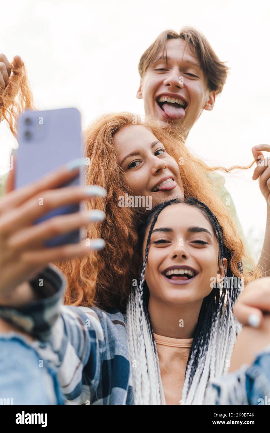 Retrato de jóvenes activos tomando un selfie juntos en una posición divertida haciendo diferentes expresiones faciales divirtiéndose juntos. Verano Foto de stock