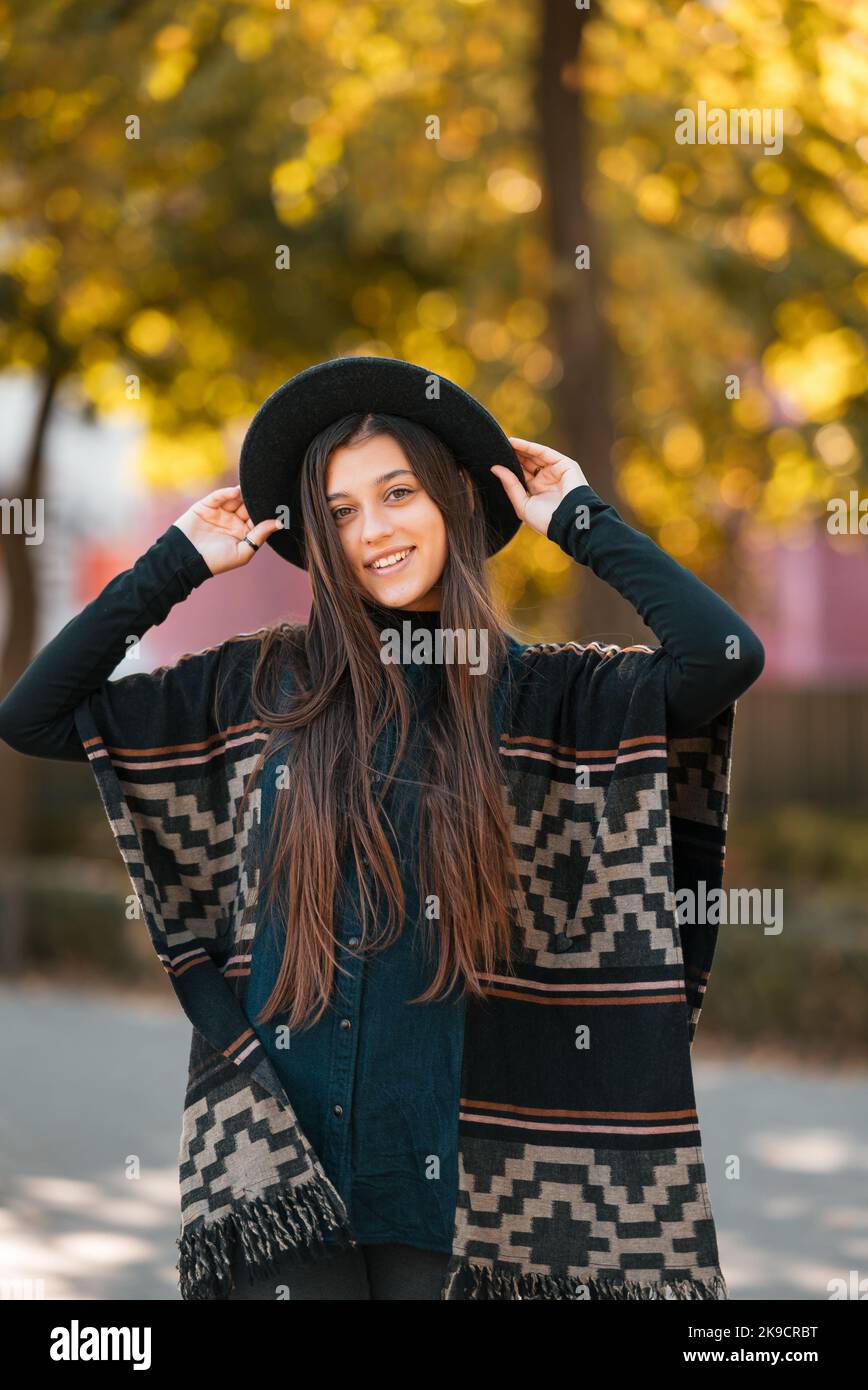 Mujer joven y bonita rubia rizada con poncho en el parque de