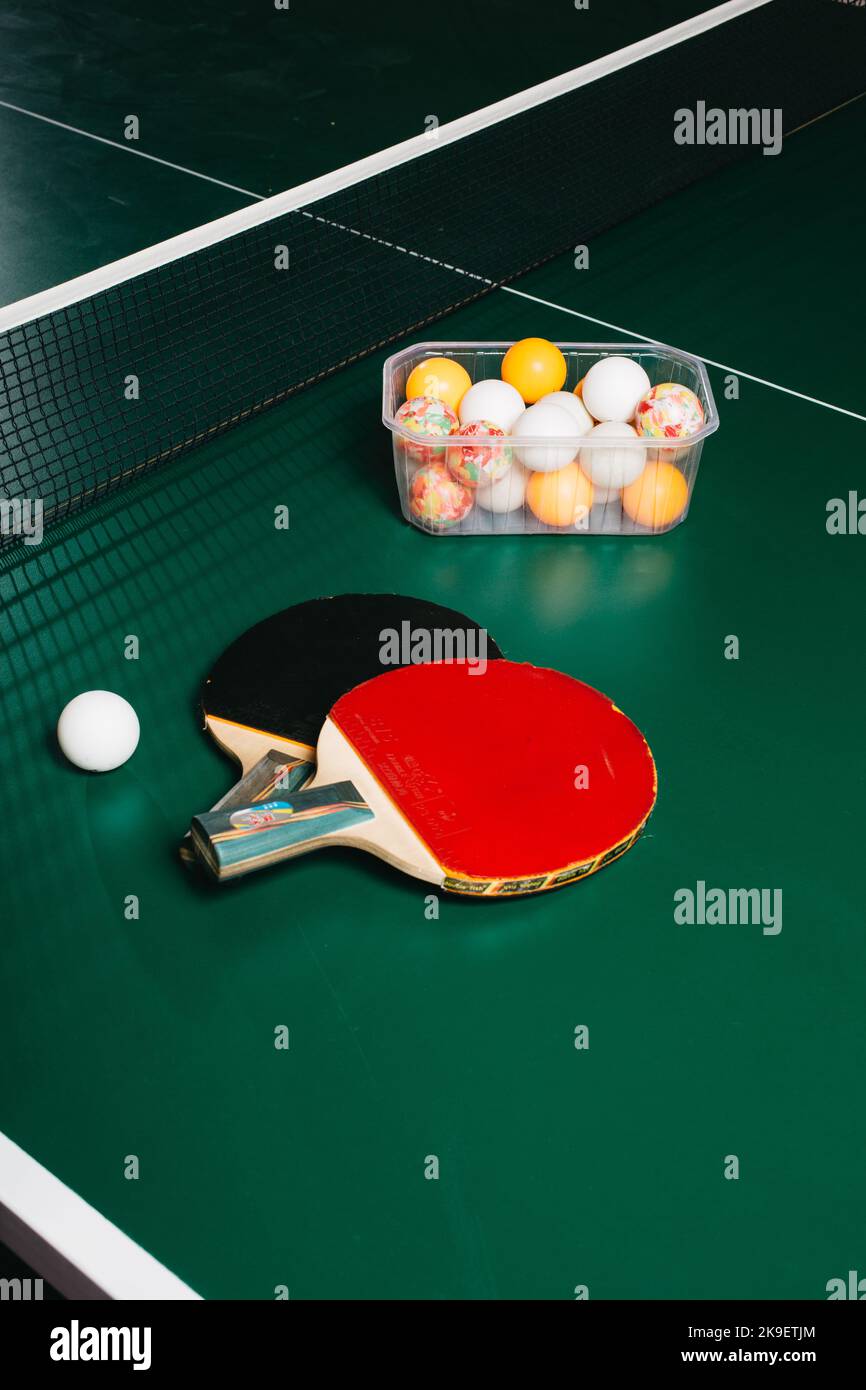 Dos raquetas de ping pong y una pelota están en la mesa de juegos verde Foto de stock