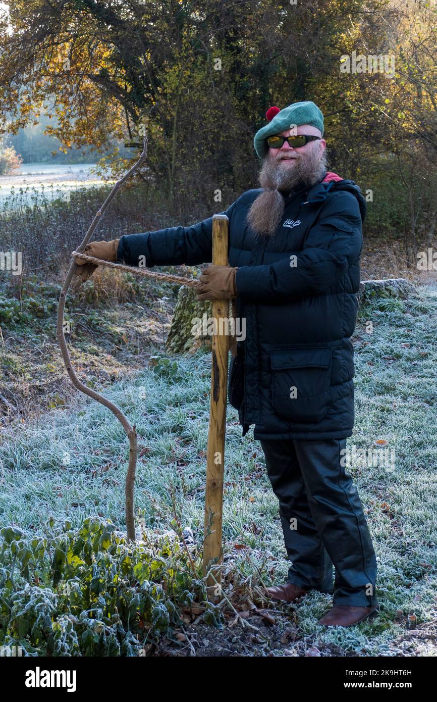 Mann mit langem Bart bindet einen krummen kleinen Baum an einem Stock fest Foto de stock