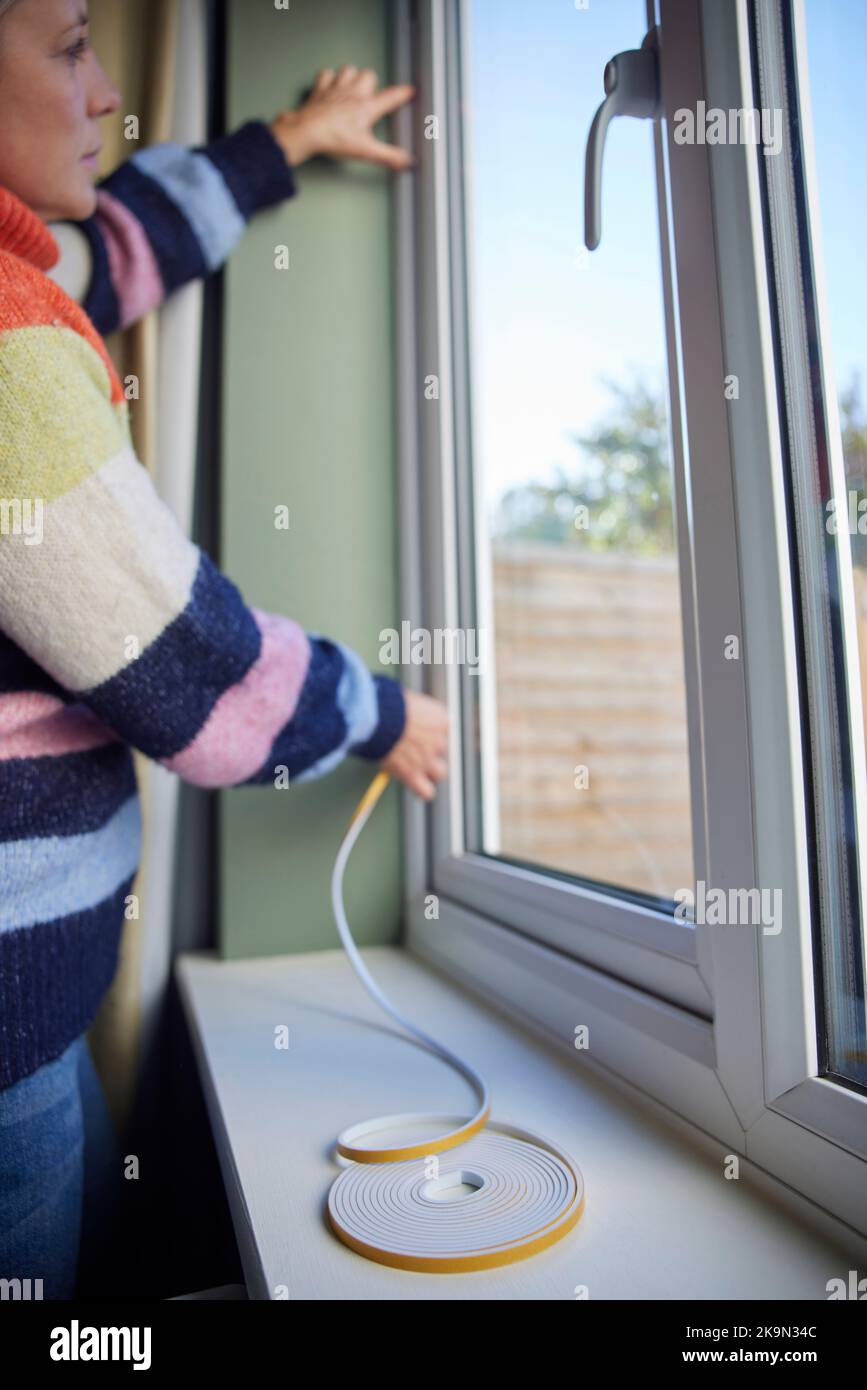 Mujer salvando enegy aislamiento Home Poniendo cinta de exclusión de draught en la ventana Foto de stock